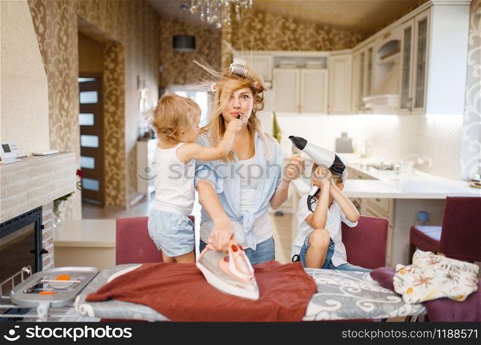Housewife and kids playing with hair dryer at the ironing board. Woman with children doing housework at home together. Female person with daughter and son having fun in their house