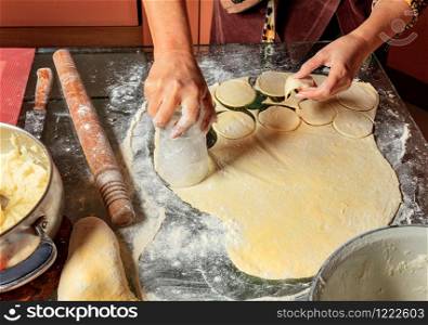Housewife hands preparing round dough pieces for modeling dumplings in Ukrainian national cuisine.. Woman molds Ukrainian dumplings. Ukrainian traditional cuisine.