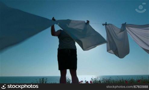 Housewife hanging white sheets on clothesline at seashore