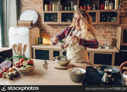 Housewife in apron cooking fresh salad, kitchen interior on background. Happy female cook. Food preparation by chef. Housewife in apron cooking fresh salad on kitchen