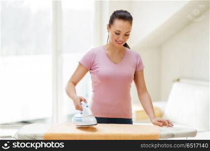 housework and household concept - happy woman or housewife ironing bath towel on iron board at home. woman or housewife ironing towel by iron at home. woman or housewife ironing towel by iron at home
