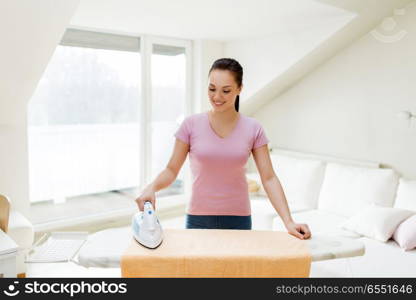 housework and household concept - happy woman or housewife ironing bath towel on iron board at home. woman or housewife ironing towel by iron at home. woman or housewife ironing towel by iron at home