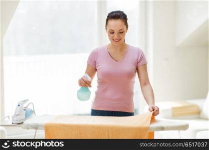 housework and household concept - happy woman or housewife spraying bath towel on ironing board at home. woman or housewife ironing towel at home. woman or housewife ironing towel at home