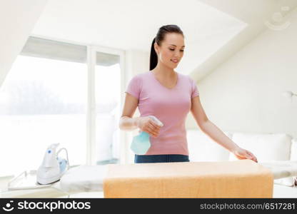 housework and household concept - happy woman or housewife spraying bath towel on ironing board at home. woman or housewife ironing towel at home. woman or housewife ironing towel at home