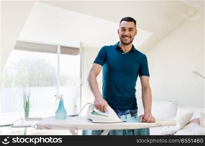 housework and household concept - smiling man ironing shirt on iron board at home. smiling man ironing shirt by iron at home. smiling man ironing shirt by iron at home