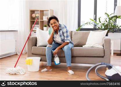 housework and housekeeping concept - african american woman or housewife with dergent, rag, bucket and mop resting after cleaning at home. african woman or housewife after cleaning at home