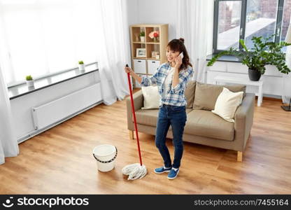 housework and housekeeping concept - happy asian woman or housewife with mop cleaning floor and calling on smartphone at home. woman with cleaning home and calling on smartphone