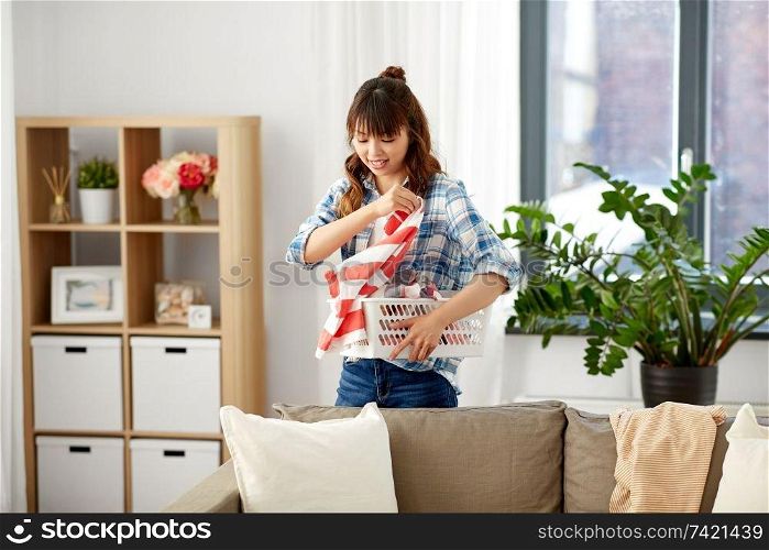 housework, cleaning and housekeeping concept - asian woman with basket picking dirty laundry at home. asian woman picking dirty laundry at home