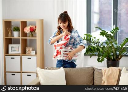 housework, cleaning and housekeeping concept - asian woman with basket picking dirty laundry at home. asian woman picking dirty laundry at home