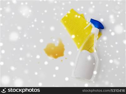 housework, housekeeping and household concept - cleaning rag, detergent spray and spilled stain on white background over snow. cleaning rag, detergent spray and spilled stain