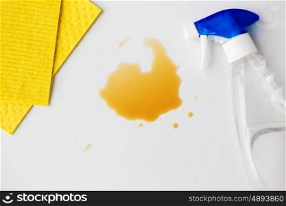 housework, housekeeping and household concept - cleaning rag, detergent spray and spilled stain on white background
