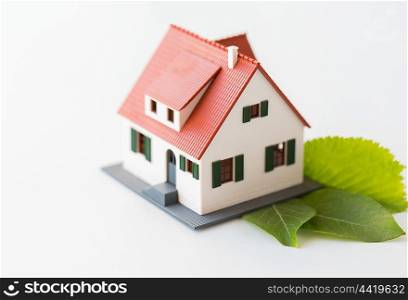 housing, environment and ecology concept - close up of living house model and green leaves