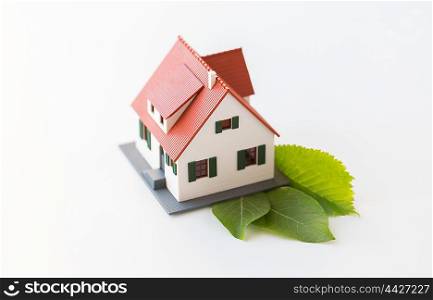 housing, environment and ecology concept - close up of living house model and green leaves