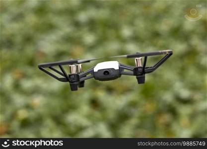 hovering black and white photo drone with four rotor blades flying in the air against a green background. hovering photo drone