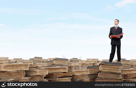 How many books have you read. Young businesman standing on pile of old books