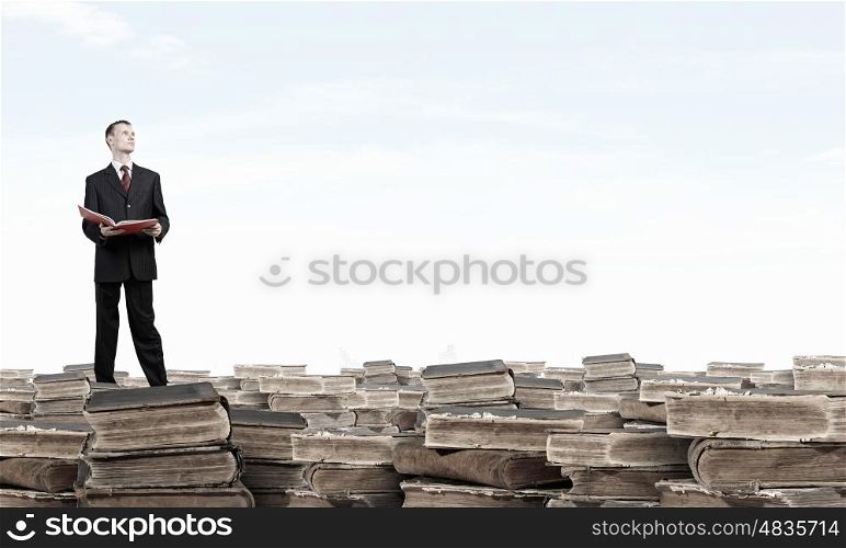 How many books have you read. Young businesman standing on pile of old books