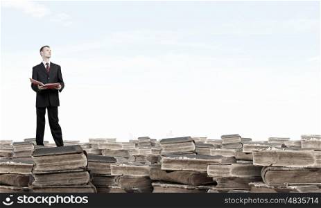 How many books have you read. Young businesman standing on pile of old books