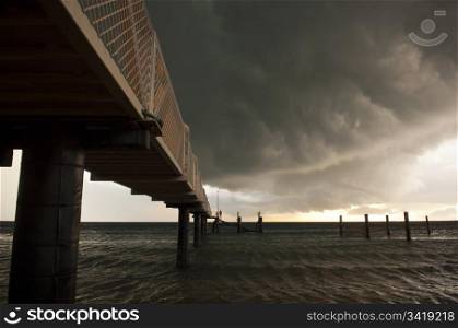 Huge black storm clouds gather as silhouetted people fish off a pier