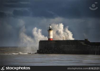 Huge sea waves crashing over lighthouse during storm with beautiful sunset light