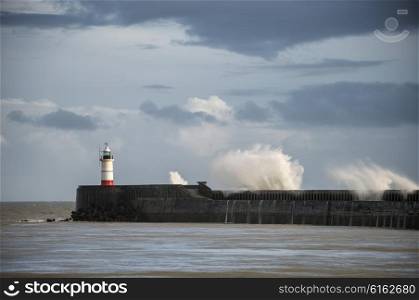 Huge sea waves crashing over lighthouse during storm with beautiful sunset light