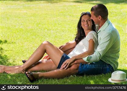 Hugging couple laughing and sitting in grass outdoors