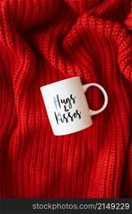 Hugs and kisses inscription on a white cup on a red knitted fabric. Love concept. St. Valentine&rsquo;s Day. Hugs and kisses inscription on a white cup on a red knitted fabric. Love concept. St. Valentine&rsquo;s Day.