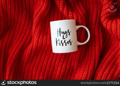 Hugs and kisses inscription on a white cup on a red knitted fabric. Love concept. St. Valentine&rsquo;s Day. Hugs and kisses inscription on a white cup on a red knitted fabric. Love concept. St. Valentine&rsquo;s Day.