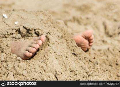Human feet buried in sand. Summer beach.. Human feet buried in beach sand. Summer holidays fun at sea.