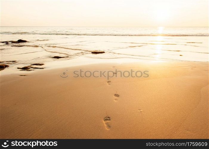 Human footprints on the golden sand beach at dusk, vanished traces of feet in the ripple waves, the sun setting on the sea backgrounds, summer scene in Lanta Island, Thailand.
