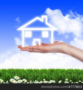 Human hand against blue sky background and house