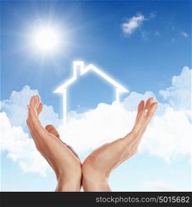 Human hand against blue sky background and house