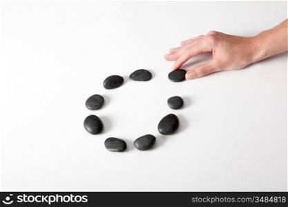 Human hand arranging line of pebbles in circle