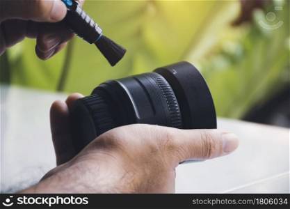 Human hand cleaning dust on camera lens with pen brush cleaner