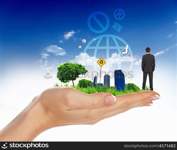human hand holding a city on green grass hill