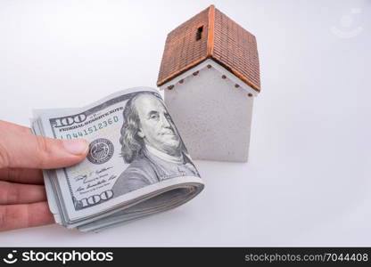 Human hand holding American dollar banknotes by the side of a model house on white background