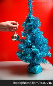 Human hand holding bauble by Christmas tree
