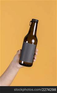 human hand holding brown beer bottle against yellow wall backdrop. High resolution photo. human hand holding brown beer bottle against yellow wall backdrop