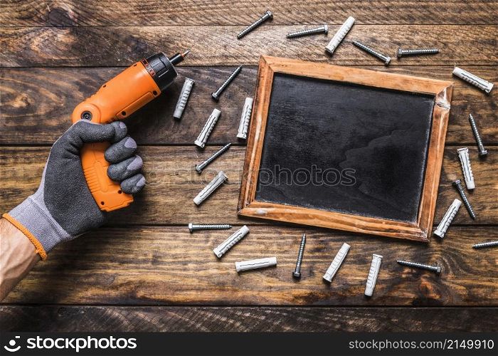 human hand holding cordless drill near screws surrounding blank slate