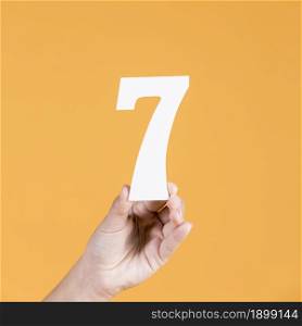 human hand holding number seven against yellow background. Resolution and high quality beautiful photo. human hand holding number seven against yellow background. High quality beautiful photo concept