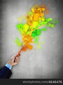 Human hand holding paint brush. Close-up of human hand holding paint brush making colorful paint splashes