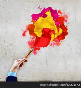 Human hand holding paint brush. Close-up of human hand holding paint brush making colorful paint splashes