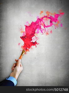 Human hand holding paint brush. Close-up of human hand holding paint brush making colorful paint splashes