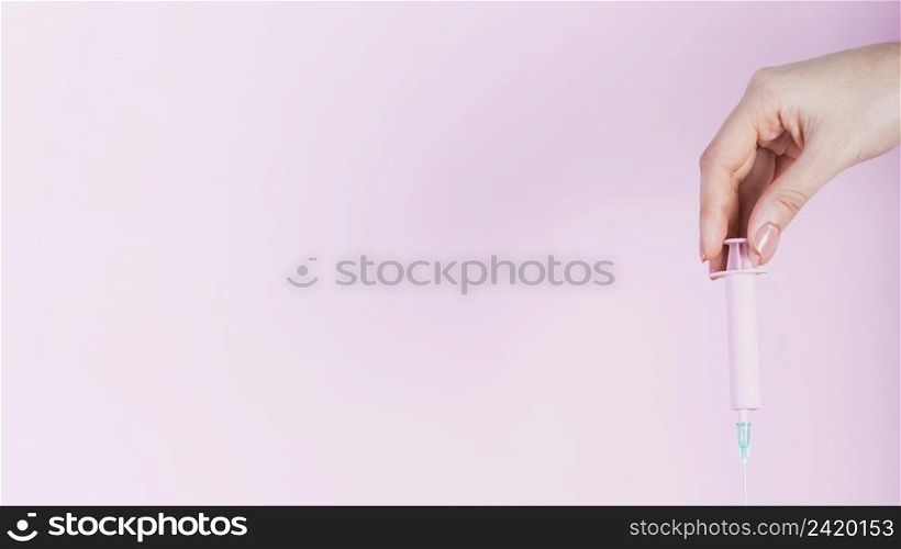human hand holding plastic syringe pink backdrop