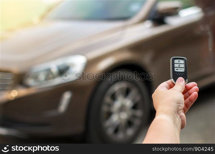 Human hand holding the car remote control against blur car.
