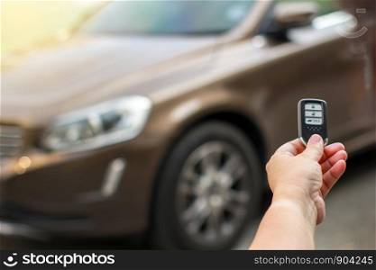 Human hand holding the car remote control against blur car.