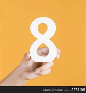human hand holding up white number 8 yellow backdrop