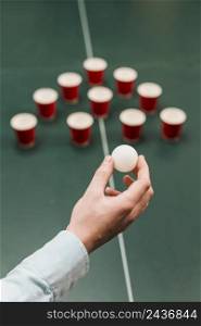human hand holding white ball playing beer pong game