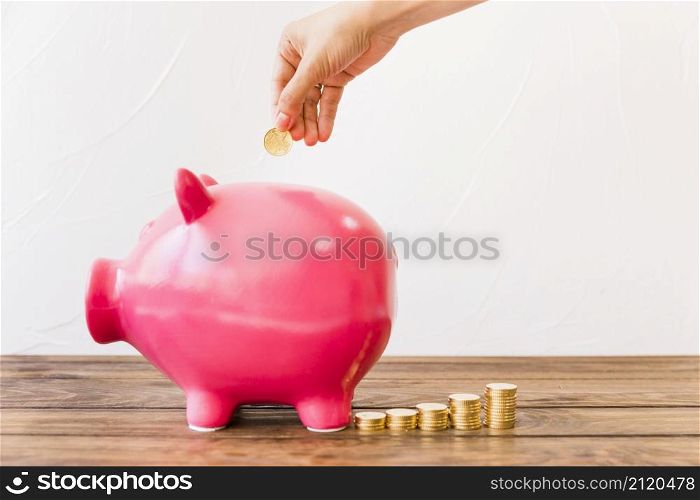 human hand inserting coin pink piggybank