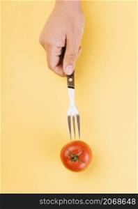 human hand inserting fork red tomato yellow backdrop