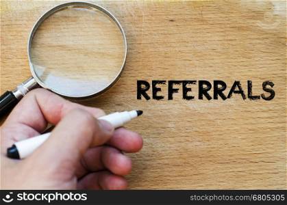 Human hand over wooden background and referrals text concept
